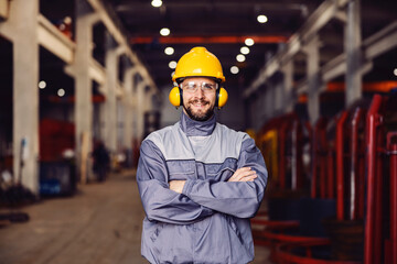 A heavy industry worker stands in a facility with arms crossed and smiles at the camera.
