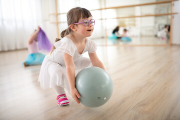 Little girl with down syndrome playing with ball at ballet class in dance studio. Concept of...