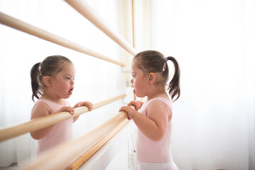 Little girl with down syndrome at ballet class in dance studio, standing in front of mirror....