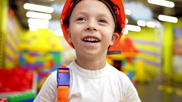 Happy boy wearing safety hardness and work helmet playing as an engineer in modern entertainment center playroom. Developing kids imagination concept.