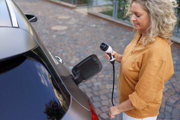 Woman holding power supply cable at electric vehicle charging station, closeup