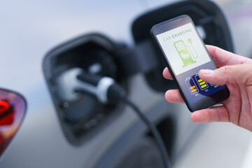 Man holding smartphone while charging car at electric vehicle charging station, closeup.