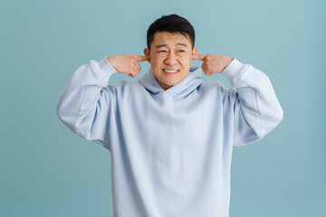 Brunette adult asian man plugging his ears with hands