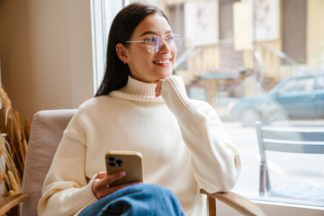 White brunette woman smiling and using mobile phone in cafe