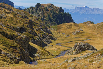 Fototapeta premium A winding creek runs between the rocks and meadows of Belledonne