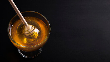 Honey in a glass bowl with honey dipper on a dark background. Space for text. Copy space