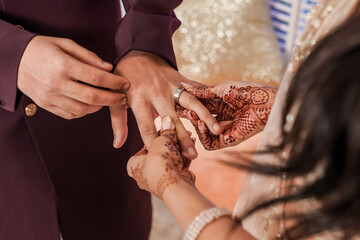 Tender hands on an Indian Bride covered with henna art holding Groom's hand while she give him an...