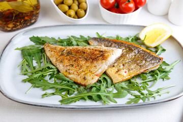 Fried dorado fillet with crispy skin. Arugula, cherry tomatoes, olives, lemon and olive oil. Traditional Mediterranean dish. White background. Selective focus, close-up.