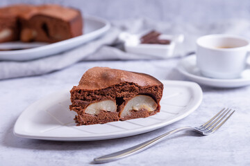 Piece of chocolate pie with pear. In the background is a pie, a cup of coffee and pieces of chocolate. Close-up.