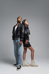 full length of stylish interracial couple standing in trendy autumnal outfits on grey.