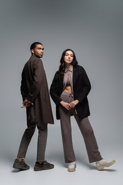 full length of stylish interracial models in trendy autumnal outfits posing together on grey.