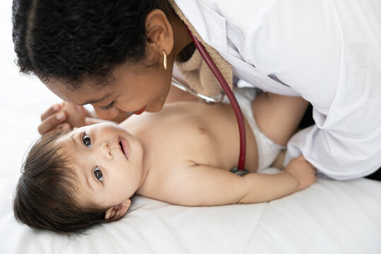 Doctor Pediatrician Examining And Kissing Baby On The Bed