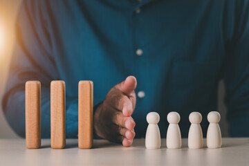 A businessman's hand protects the wooden domino so that it does not fall on the wooden doll....
