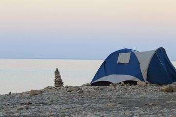 a tourist tent of blue color on the seashore, and next to the stones, a folded pyramid
