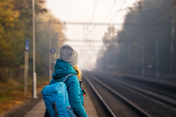 Tourist with backpack wait for train on station. Travel at fall season