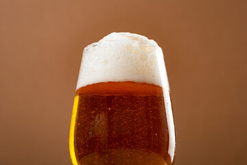 One glass amber golden beer overflowing against brown  background