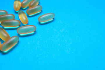 Capsules of fish fat oil, omega 3, vitamin e on the blue background with copy space. Healthcare, vitamins, supplements daily intake concept.