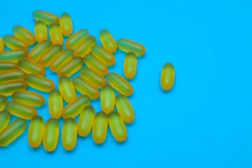 Capsules of fish fat oil, omega 3, vitamin e on the blue background with copy space. Healthcare, vitamins, supplements daily intake concept.