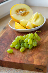 a plate of melon slices, green grapes on a wooden background, kitchen windowsill, concept of fresh fruits and healthy food