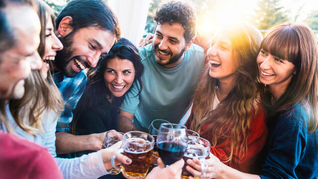 Happy young people enjoying happy hour drinking at bar restaurant terrace - Group of friends toasting beer and wine glasses together - Beverage and friendship concept with laughing guys and girls