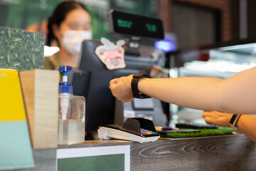 Woman paying bill through smartwatch using NFC technology in cafe.