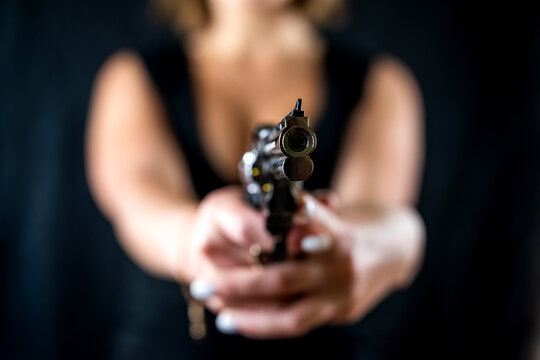 serious woman in stylish clothes posing faceless with revolver gun isolated on black background