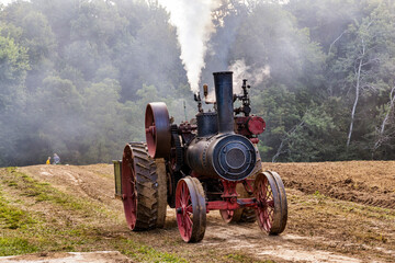 Old steam engine moving through rural farm field.