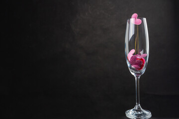 Champagne glass filled with sequin hearts. Copy space on black background.