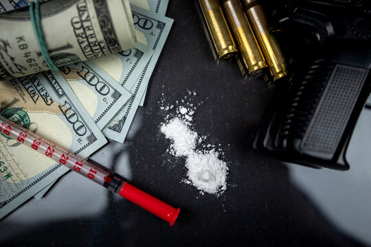 gun with bullets and a syringe and drugs in the form of powder lie on a black table.