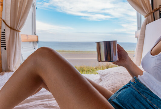 Detalle de mujer irreconocible con la taza en la mano, acostada en la cama de la camper, con vistas al mar. Fotograf&iacute;a horizontal con copy space.