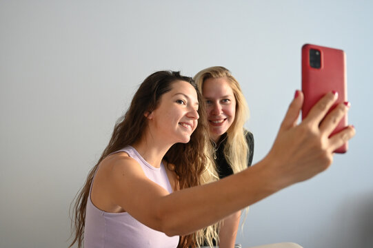Young smilling women making selfie on the light room. Portrait of two young woman taking a selfie