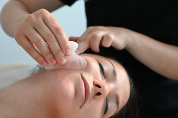 Obraz na płótnie Canvas Cosmetologist does a facial massage with a gouache scraper. close up. Professional anti-aging facial massage.