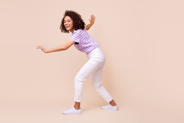 Fototapeta na wymiar Full size photo of positive lovely girl dressed striped t-shirt white trousers sneakers sneaky walk isolated on beige color background