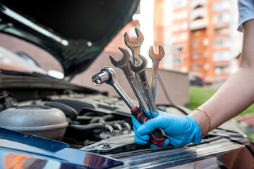car mechanic repairs a car engine near a car with an open hood.