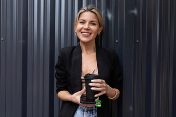 successful woman office employee with a mobile phone and a cup of tea on the background of a gray wall looks at the camera with a smile