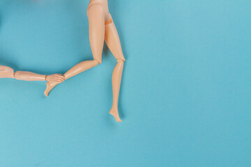 Top view doll hand touching womans leg. Blue background with copy space. - obrazy, fototapety, plakaty
