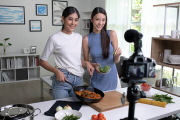 Young Asian lesbian couple blogger influencer vlogger shooting video in kitchen. LGBT couple live-...