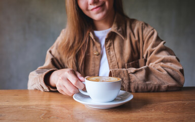 Closeup image of a young woman holding and drinking hot coffee in cafe