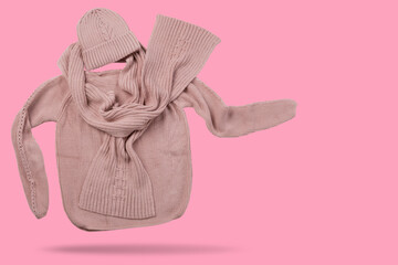 A sweater, a scarf and a knitted hat, like a walking person, a scarf is developing, a concept, on a pink background