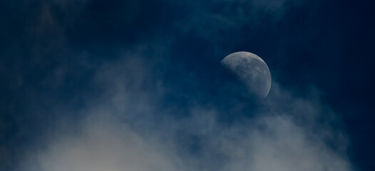 Fototapeta na wymiar Half moon and dramatic thin cloud in a dark blue tone