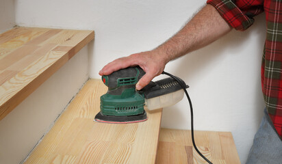 Closeup of worker hand sanding wooden stairs using  power tool