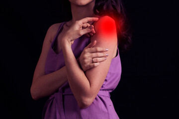 young woman experiencing pain in the shoulder joint on black background.