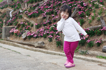 An Asian kid in a white shirt and purple pants in action with a smiley face in natural daylight. An Asian girl kid with rocks in the background.