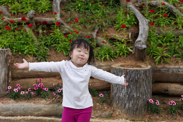 An Asian kid in a white shirt and purple pants in action with a smiley face in natural daylight. An Asian girl kid with woods and rocks in the background.