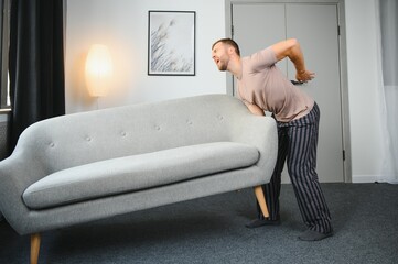 Obraz premium Young man suffering from back pain after carrying heavy furniture.