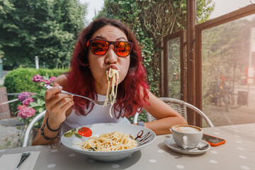 The girl is in a funny hurry and eats Italian pasta in a cafe. The concept of good manners and...