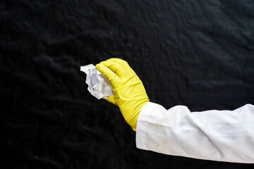 A doctor in a medical gown and protective gloves holds a crumpled sheet of paper in his hand. The face is not visible. Concept - pollution with waste and garbage.