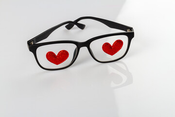 Close up glasses with red hearts atteched to lenses. White reflective background.
