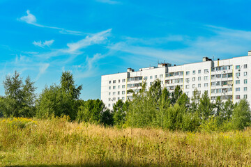 Fototapeta na wymiar The upper floors of an apartment building behind trees against a blue sky.