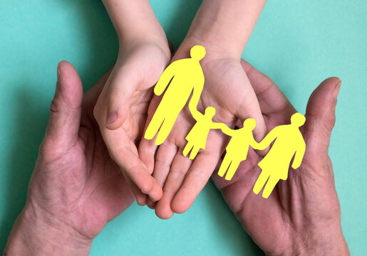 the hands of a man and a child hold a silhouette of a family with children cut out of yellow paper. The concept of family traditions and values, succession of generations. Family with small children